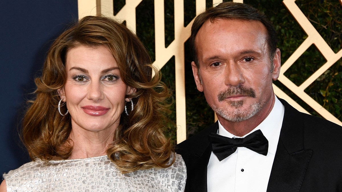 Faith Hill in a sparkly dress soft smiles next to Tim McGraw in a classic tuxedo looking more serious