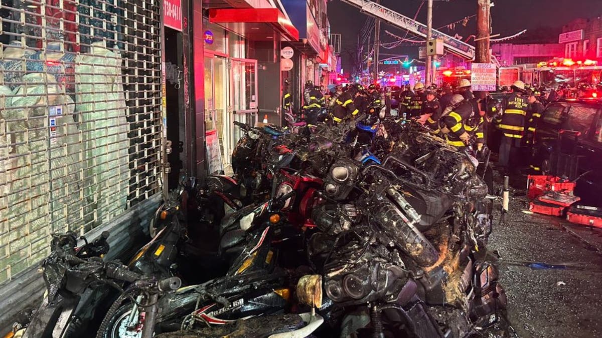 A night time image of a number of charred e-bikes and mopeds are seen outside a bike store which burned down