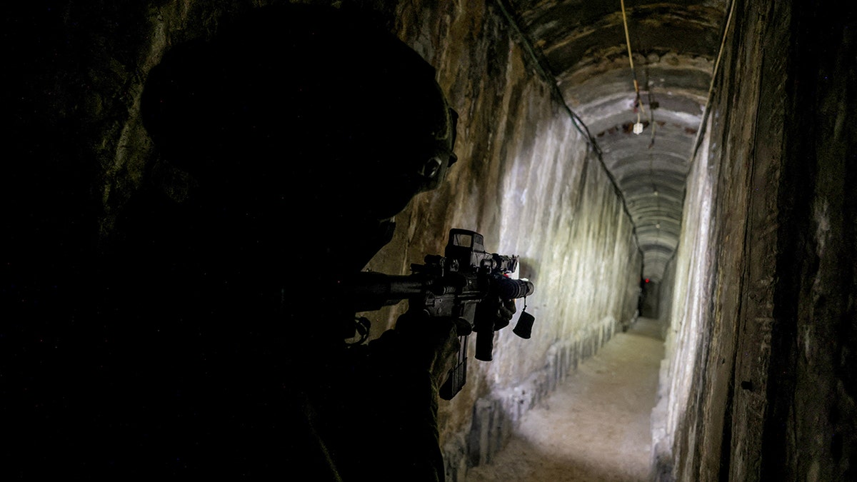 An Israeli soldier shines a light on his rifle down a Hamas tunnel