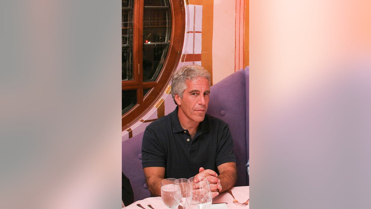 Jeffrey Epstein sitting at a dinner table and wearing a black polo shirt