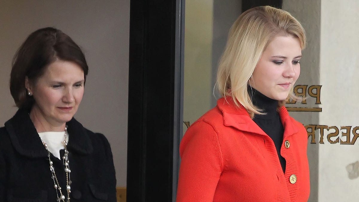 Elizabeth Smart wearing a red coat walking in front of her mother Lois in a black sweater and white shirt