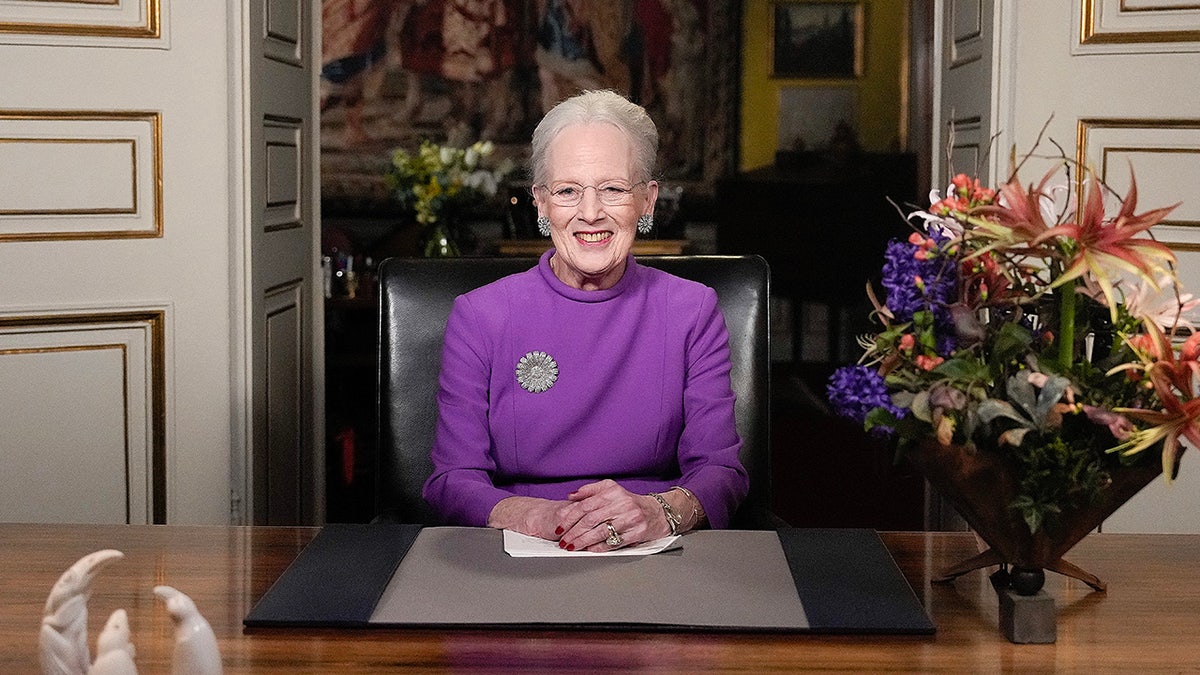 Queen Margrethe wearing a purple dress and sitting in front of her desk