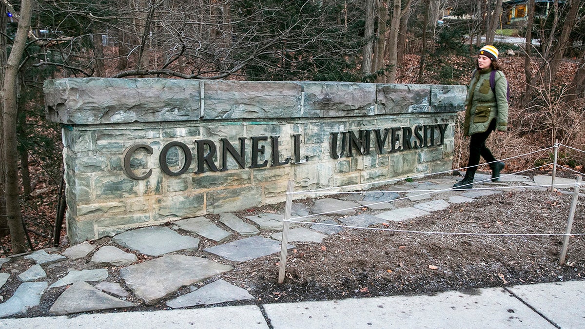 Cornell University sign shown with woman walking by