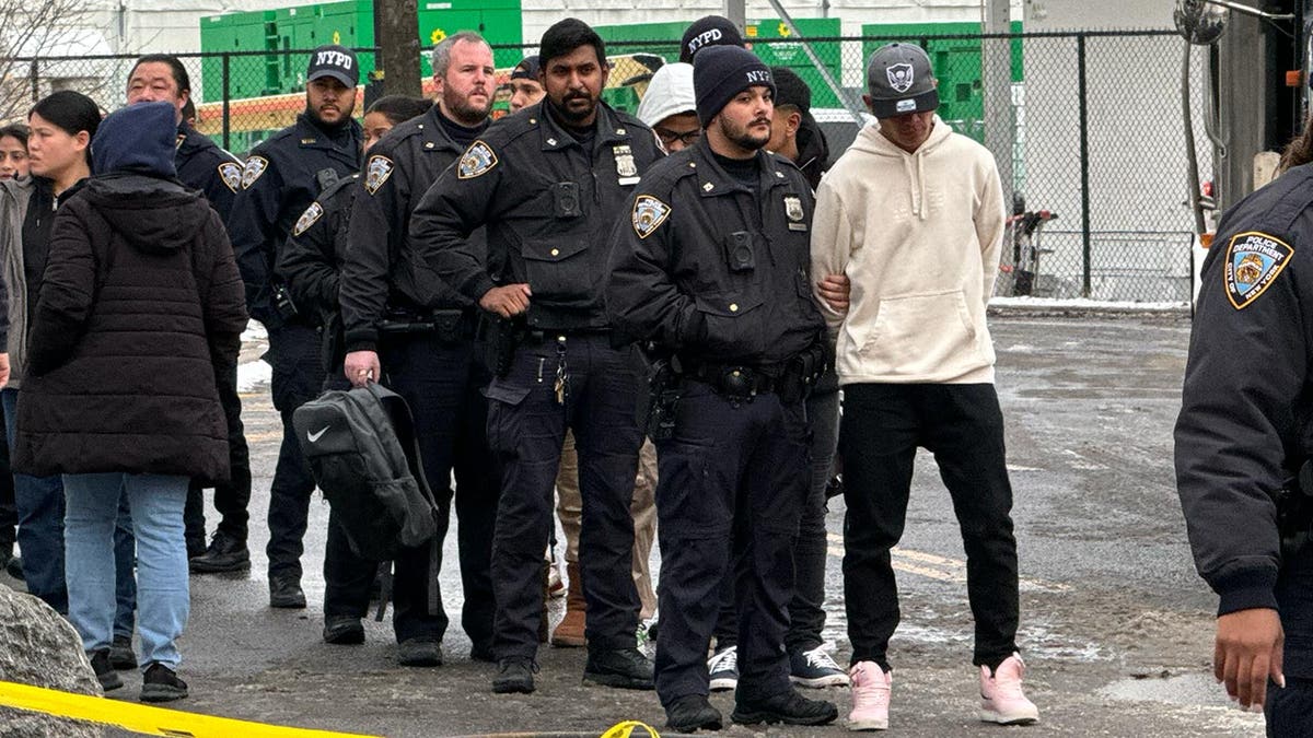 Migrant in handcuffs being led by NYPD police