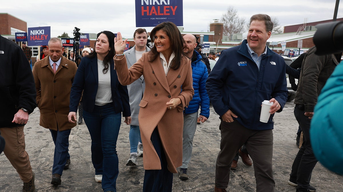Nikki Haley waving and New Hampshire Gov. Chris Sununu walking with other men and women by supporters
