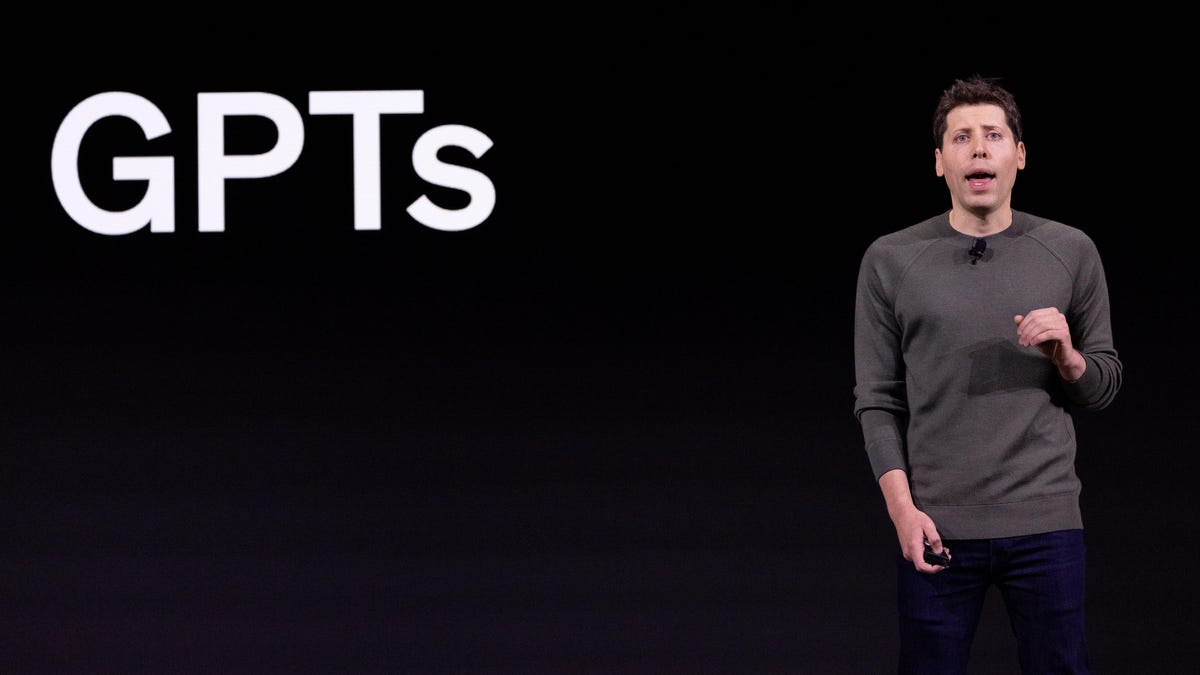 OpenAI CEO Sam Altman stands in front of a black screen that shows the term "GPTs" in bold white letters during a developer event in November 2023.