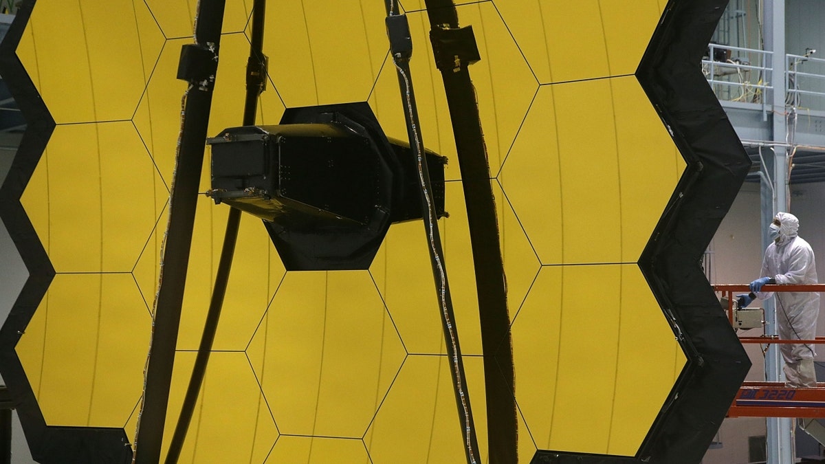 A technician stands next to the James Webb Space Telescope