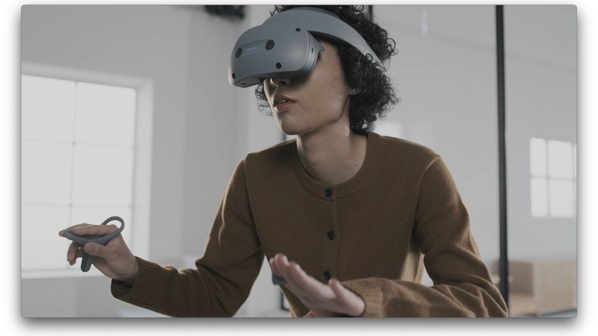 A woman wearing a flip-down grey VR headset with a ring and controller in hands
