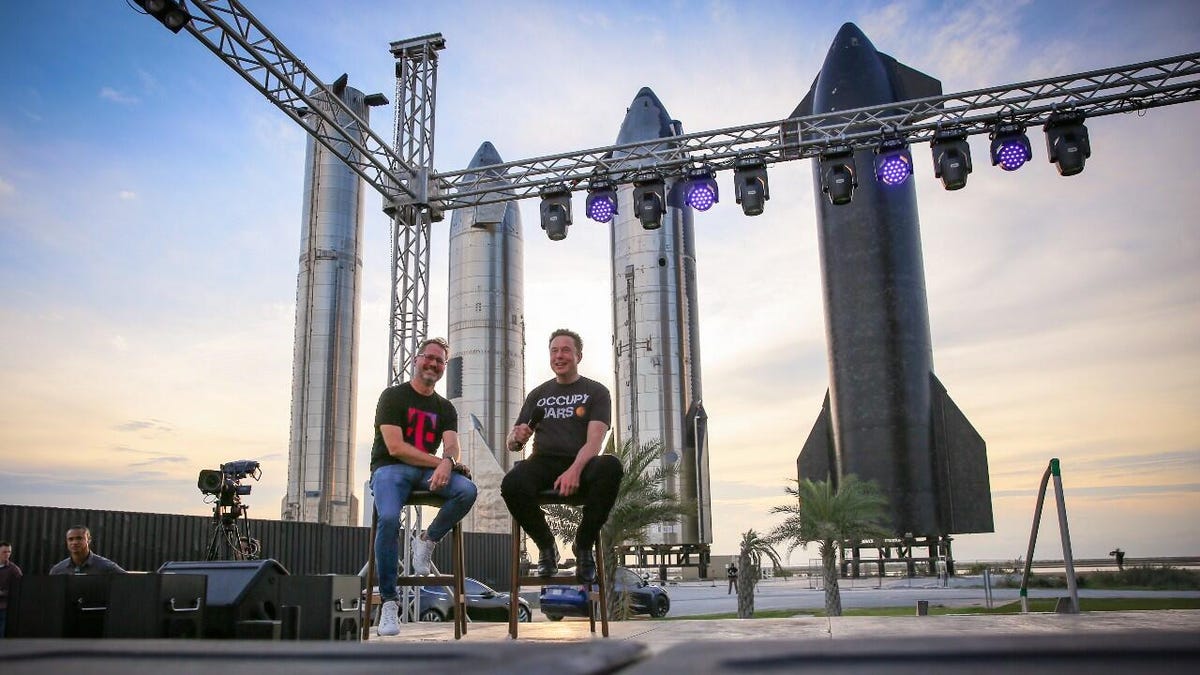 Mike Sievert and Elon Musk in T-shirts on an open-air stage with SpaceX rockets in the background