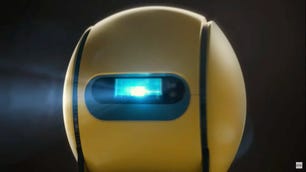 Samsung Ballie robot: a yellow sphere with two vertical black indentations running top to bottom on either side of a horizontal window that houses a projector. The projector's blue-white beam streams forth.