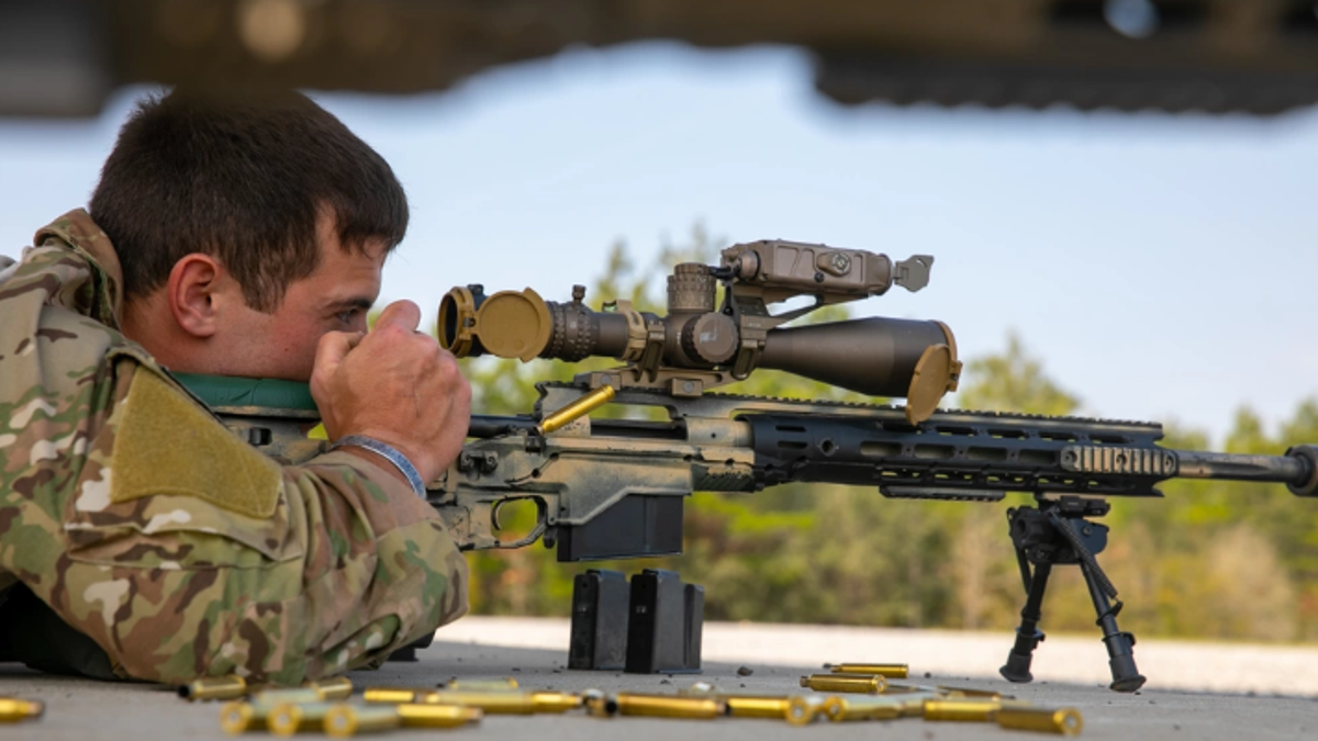 Army soldier looks through scope of sniper rifle
