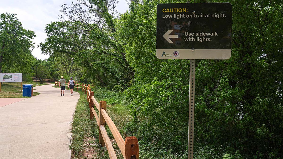 A sign warns of poor lighting conditions at night on a hike and bike trail along Lady Bird Lake