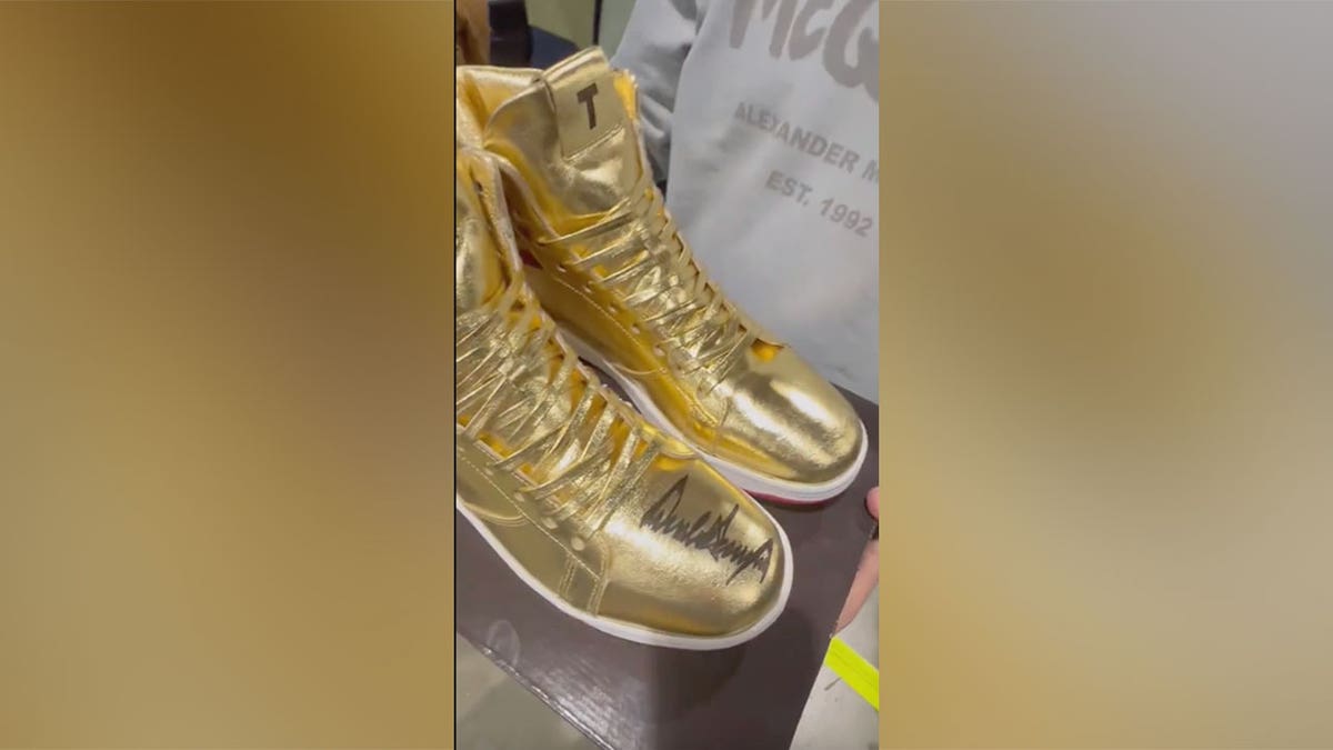 CEO Roman Sharf holds out and displays gold signed Donald Trump sneakers
