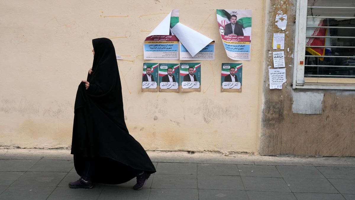 A woman walks past electoral posters of candidates in Iran