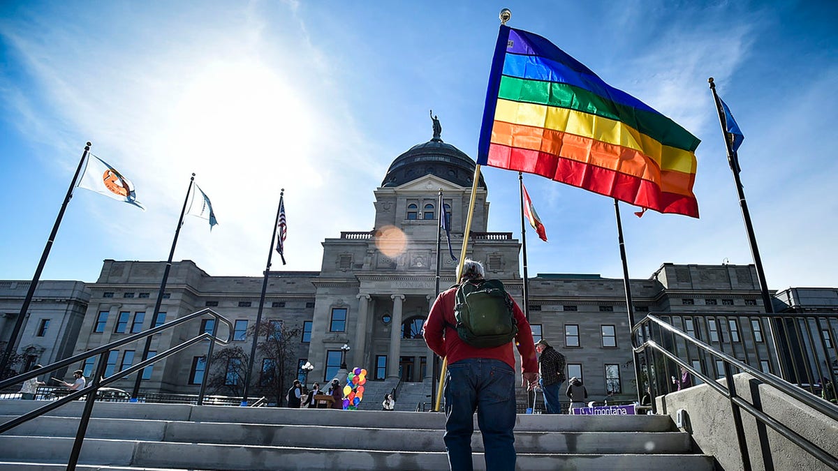 man carries rainbow flag up stairs outside Kansas state capitol