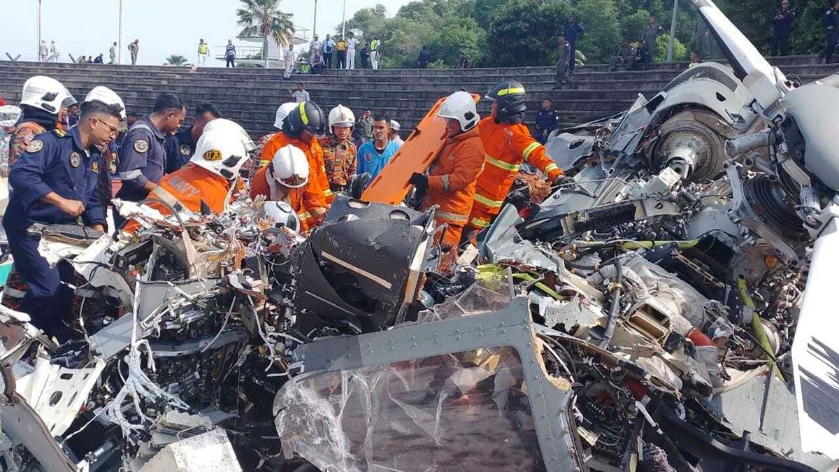 Teams from the fire and rescue department dressed in orange or blue jumpsuits inspect the twisted wreckage of two helicopters in Lumur, Malaysia