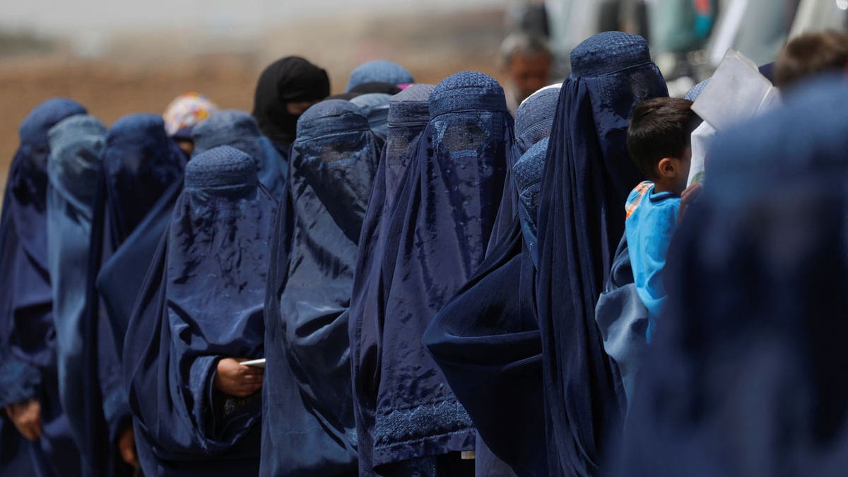 Displaced Afghan women stand waiting to receive cash aid