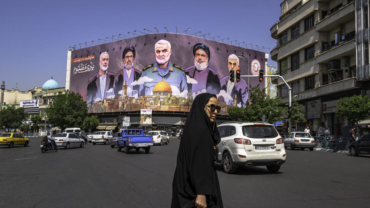 Cars passing, people moving past a large banner featuring portraits of slain leaders from Iran-aligned armed groups
