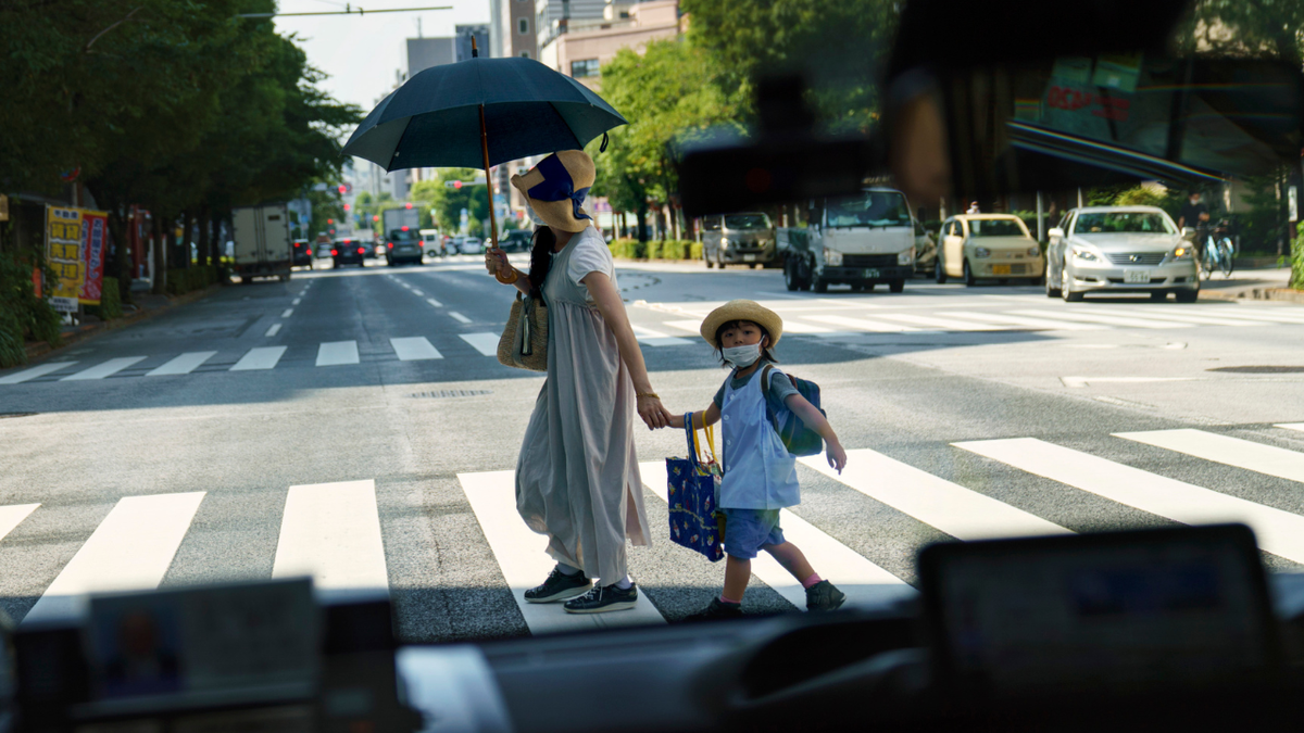 A pedestrian crossing a street with a child is seen through a taxi window in Tokyo, Monday, July 19, 2021.