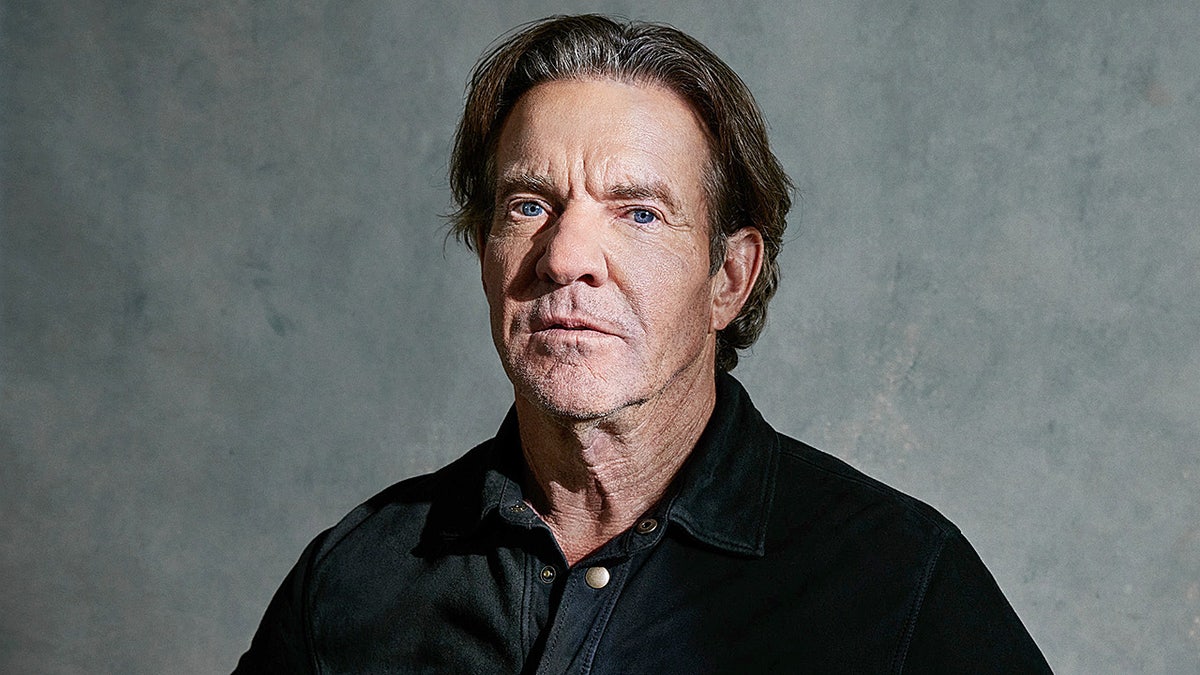 Dennis Quaid in a black shirt looking at camera