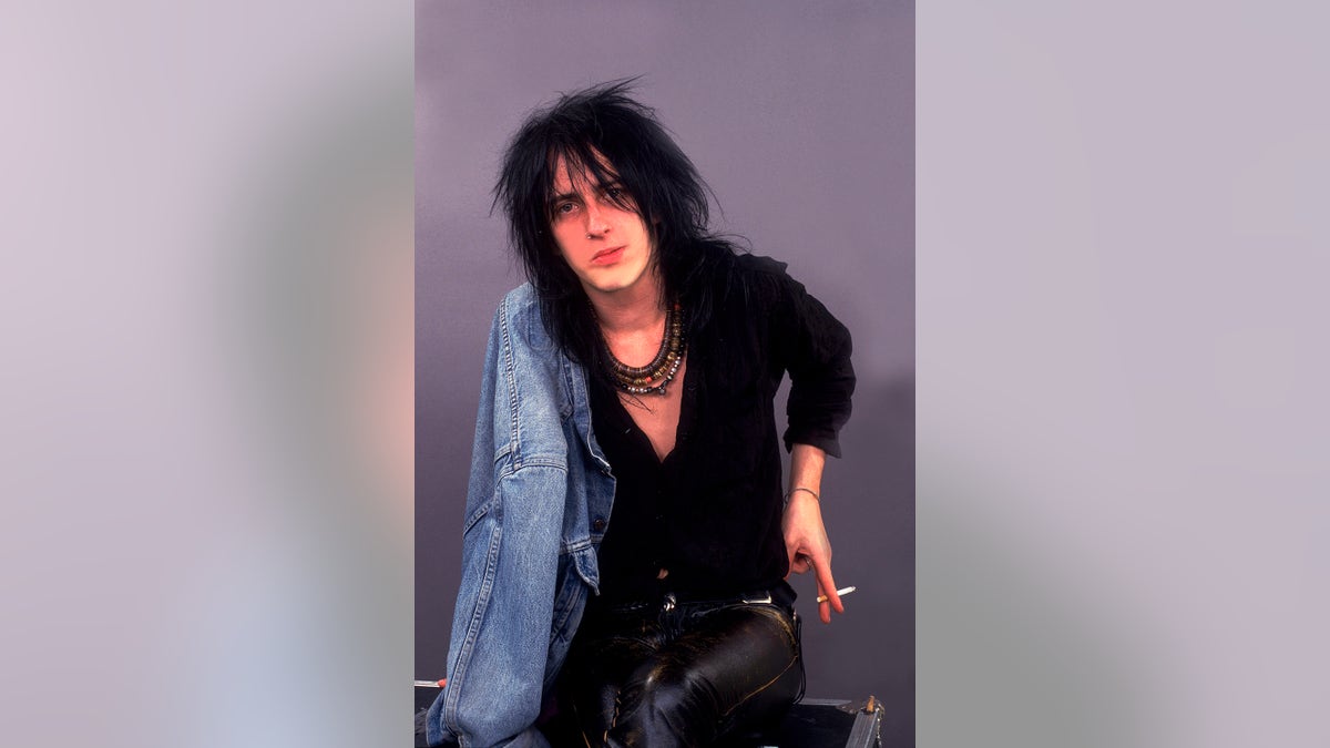 Izzy Stradline wearing all black with a jean jacket as he holds a cigarette.