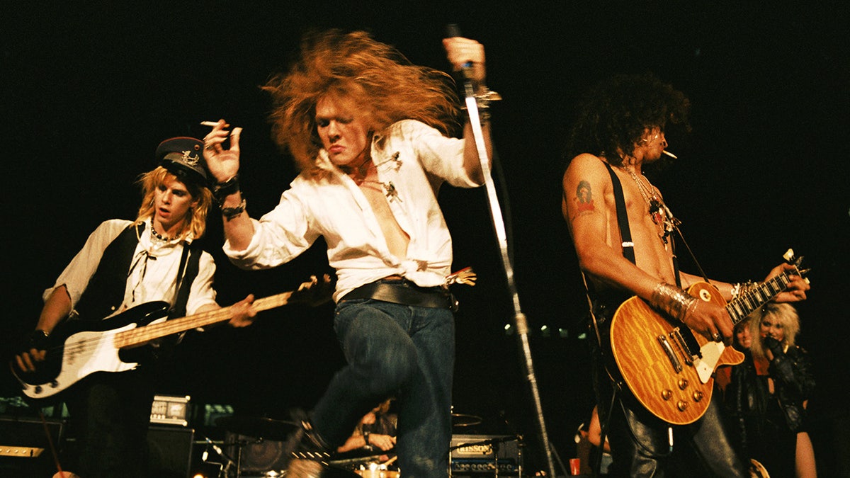 Axl Rose jumping on stage and performing with his bandmates.