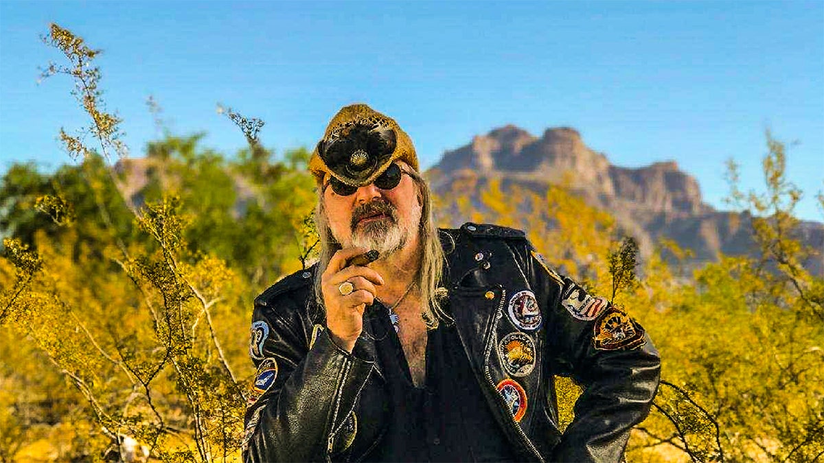 Alan Niven smoking a cigar with a cowboy hat out in the field.
