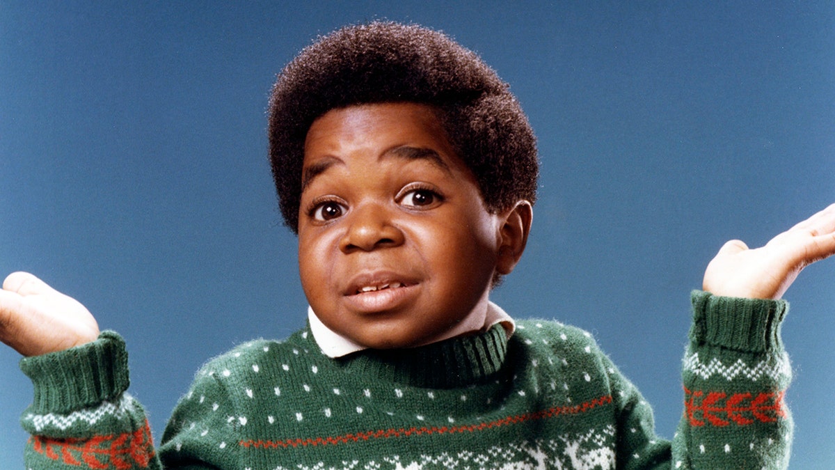 A young Gary Coleman with his green sweater shrugging his hands.