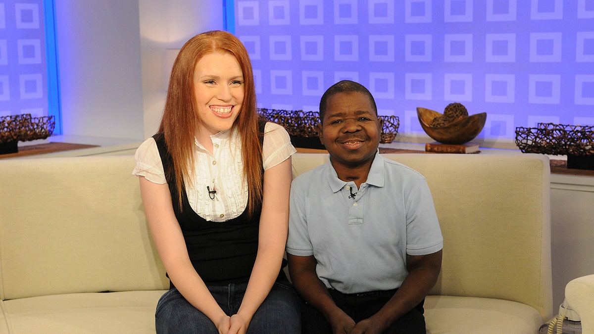 Shannon Price wearing a black vest and a white shirt smiling and sitting next to Gary Coleman in a grey shirt.