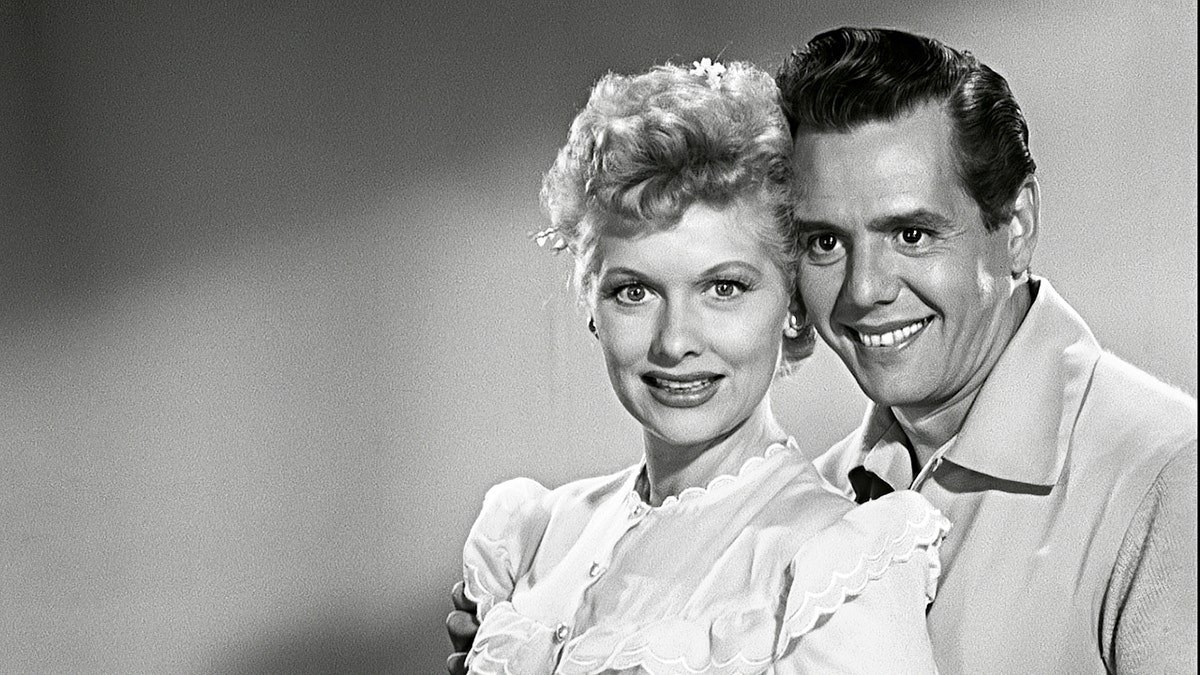 Lucille Ball wearing a white nightgown leaning on her smiling husband Desi Arnaz.