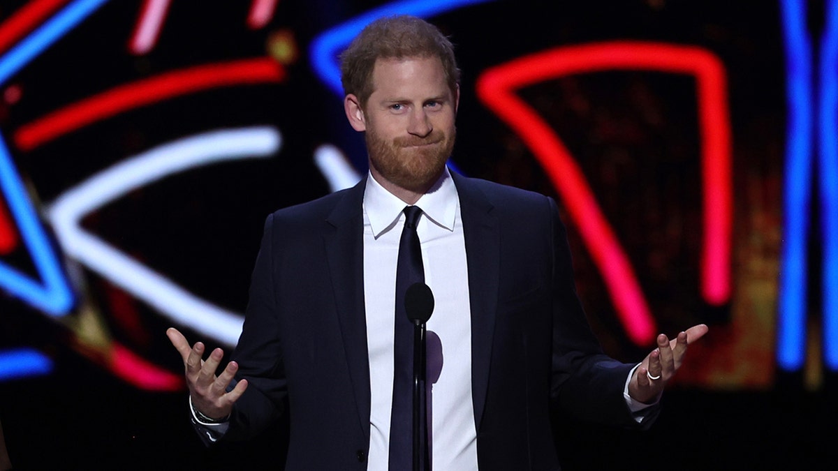 Prince Harry shrugging in a suit and tie on stage.