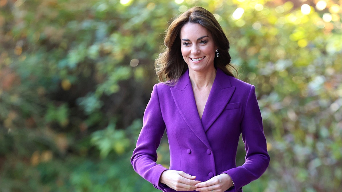Kate Middleton wearing a purple suit and smiling.