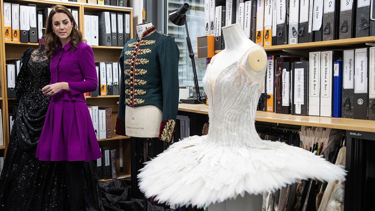 Kate Middleton wearing a purple dress looking at a white ballet costume.
