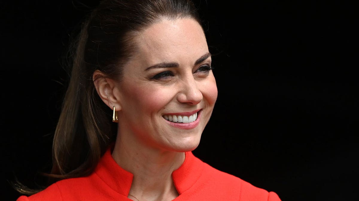 Kate Middleton smiles for a photo in a red coat