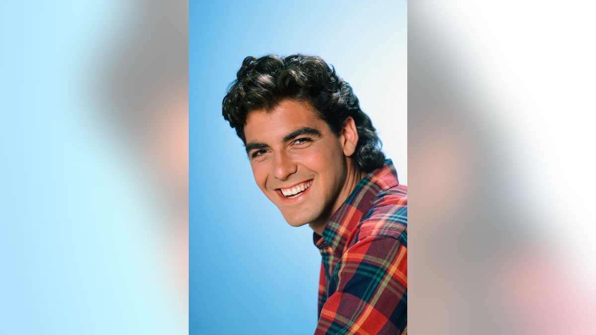George Clooney smiling wearing a plaid shirt.