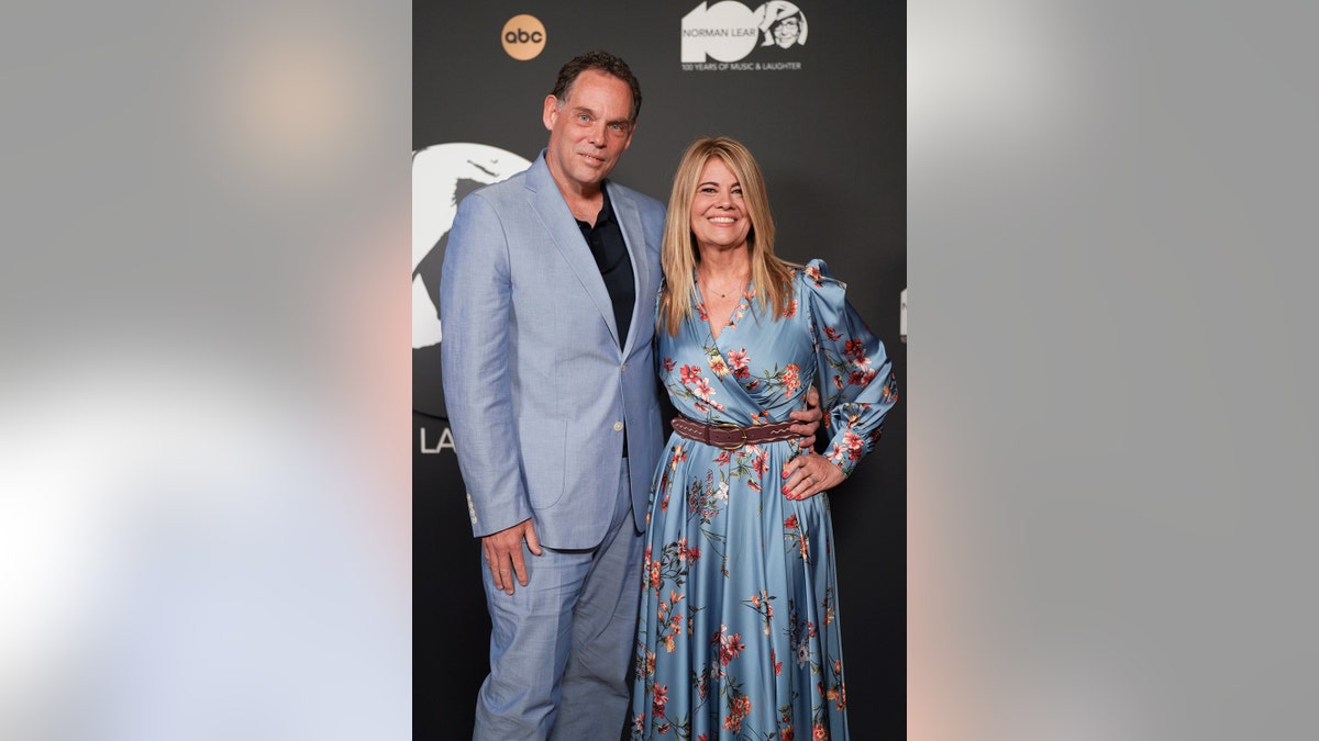 Lisa Whelchel in a light blue floral dress posing with her husband in a matching suit.