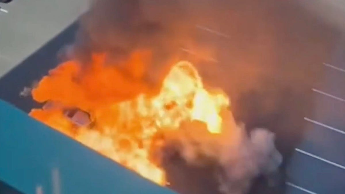 A silver vehicle exploding into a fireball in a parking lot