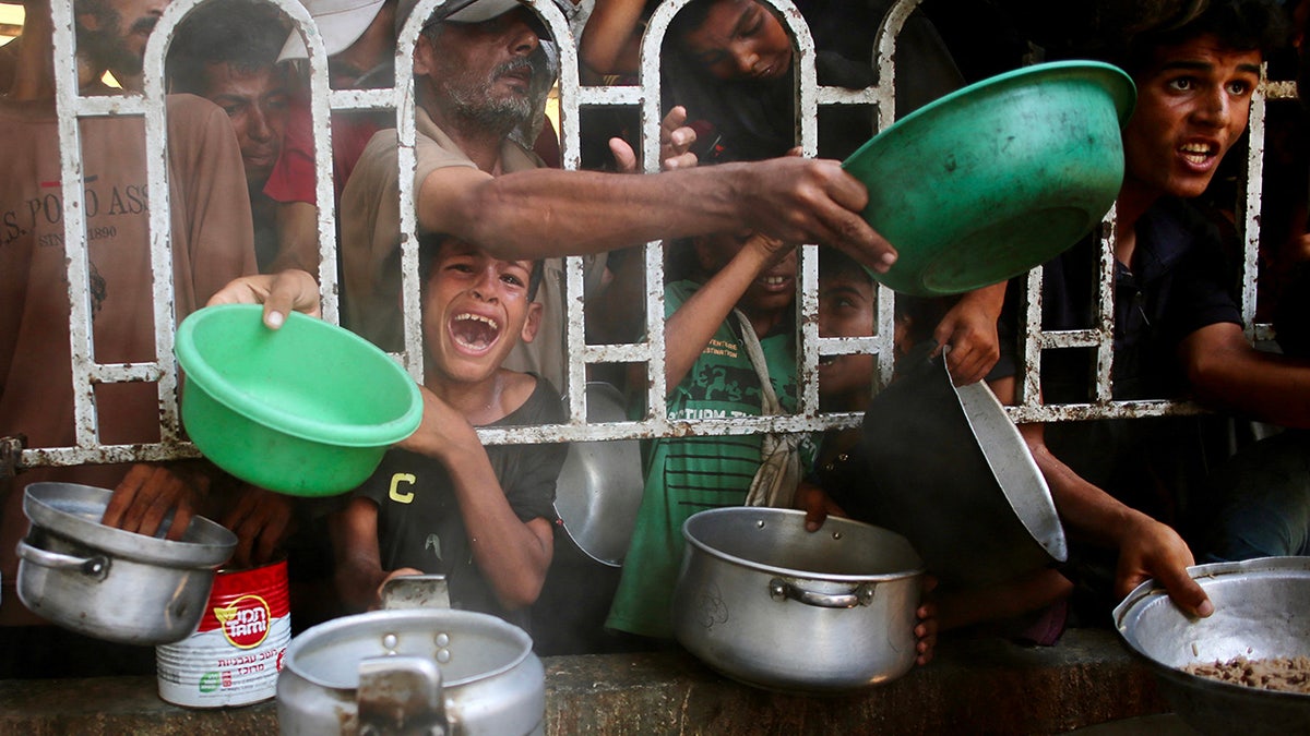 Gazans with arms outstretched holding bowls, trying to get food