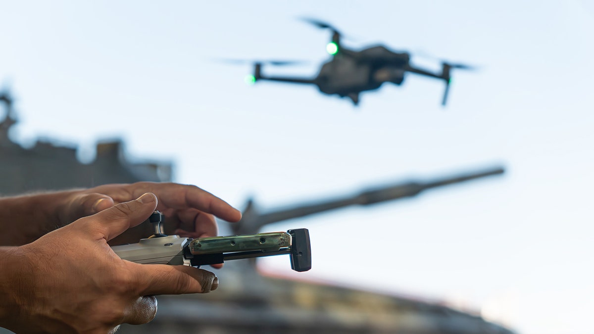 A person holding a controller while a drone flies in the background