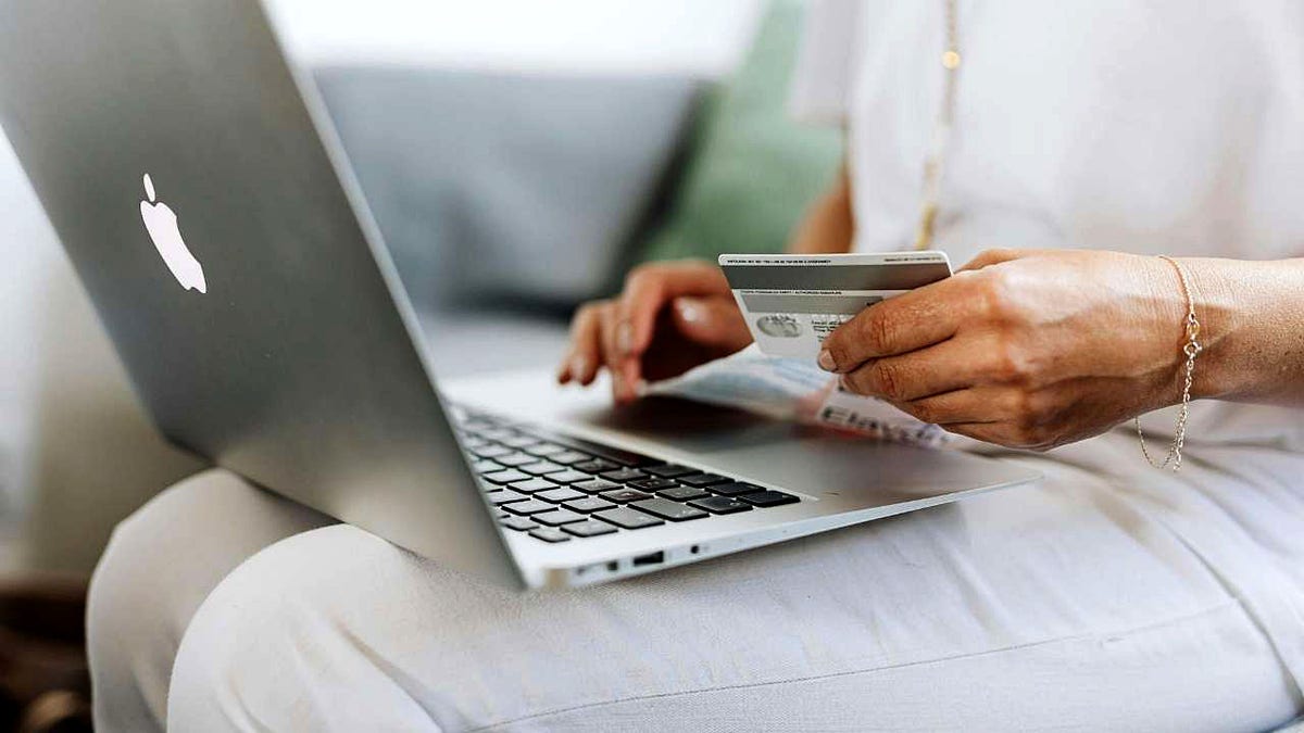 A woman holds a credit card as she types on her laptop.