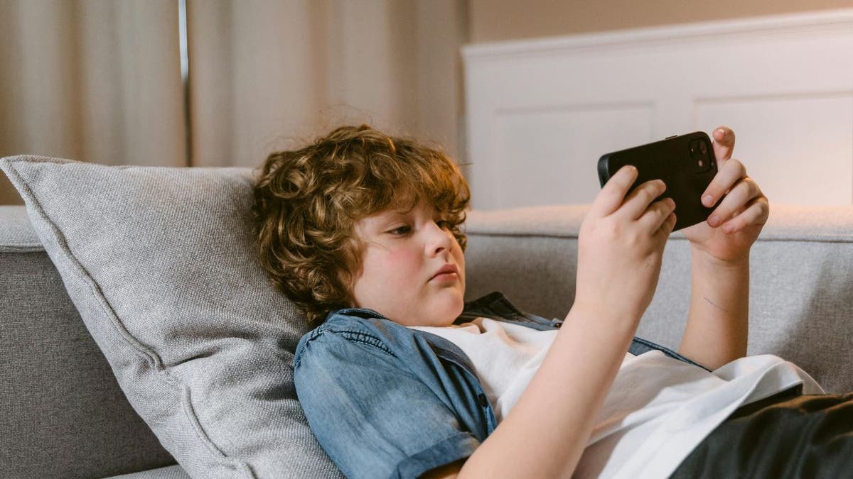 Child using a device on a couch.
