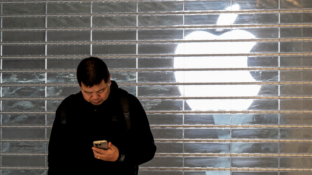 A man looks at his phone in front of an Apple logo