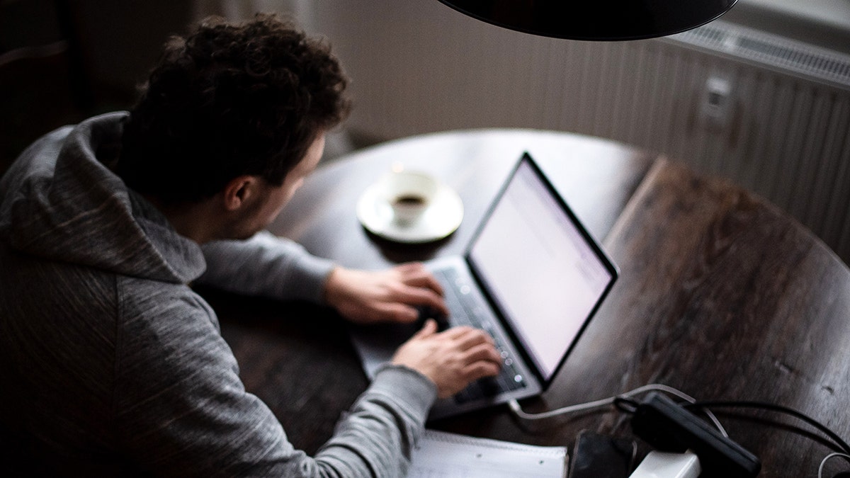 Man sitting at his table while typing into her laptop.