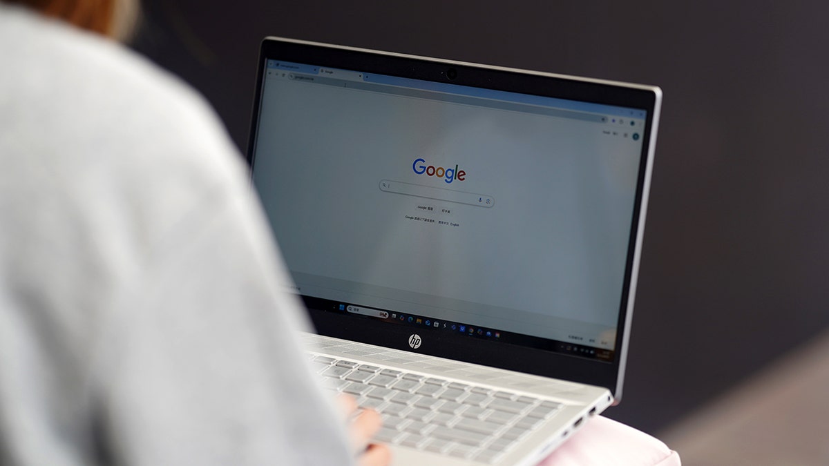 A person uses a laptop with a Google search tab open on the screen.