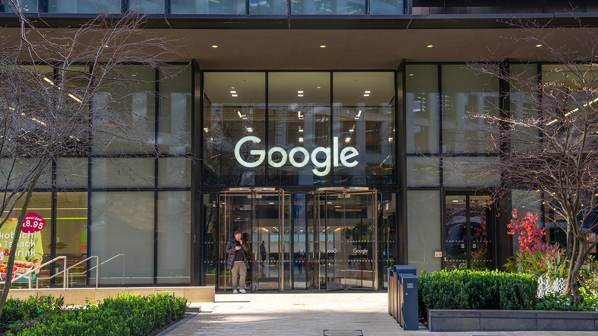 A man stands in front of a building with a Google sign over the doors.