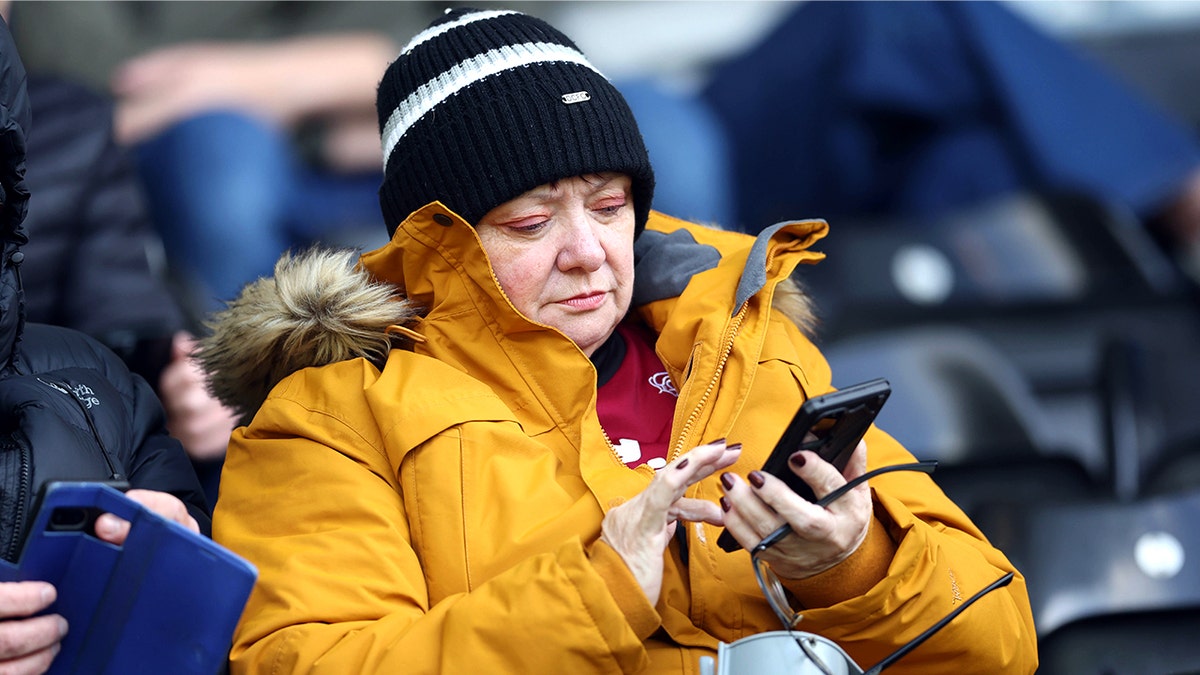 A woman in a yellow jacket uses an android smartphone.