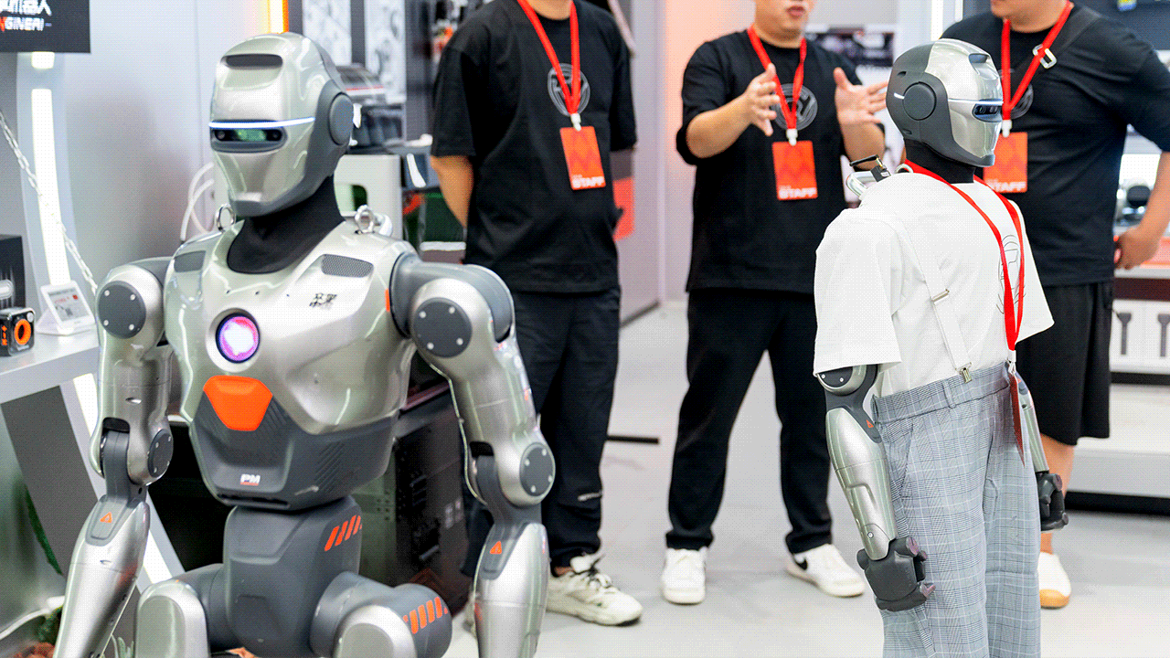 Two EngineAI PM01 humanoid robots stand as men with red badges gesture toward them.