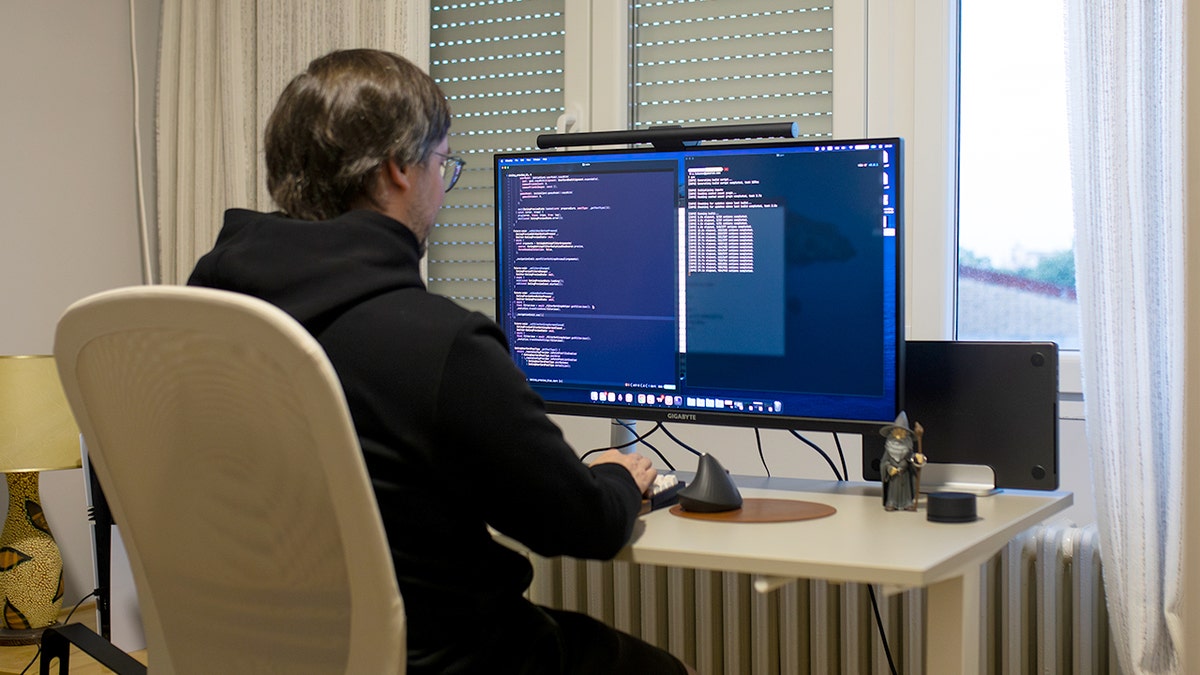 A man sits in front of a desktop computer with code on the monitor.
