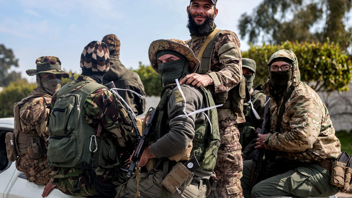 Security forces loyal to the interim Syrian government ride in the back of a vehicle moving along a road in Syria's western city of Latakia on March 9, 2025